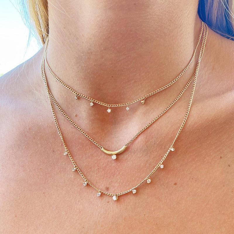 woman's neck wearing a Zoë Chicco 14k Gold 5 Dangling Diamond Extra Small Curb Chain Necklace layered with two other prong diamond necklaces