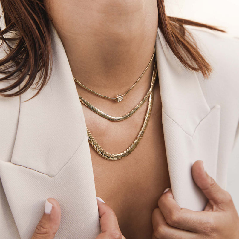 angled view of a woman holding the lapels of her cream blazer wearing a Zoë Chicco 14k Gold Large Emerald Cut Diamond Snake Chain Necklace layered with two snake chain necklaces