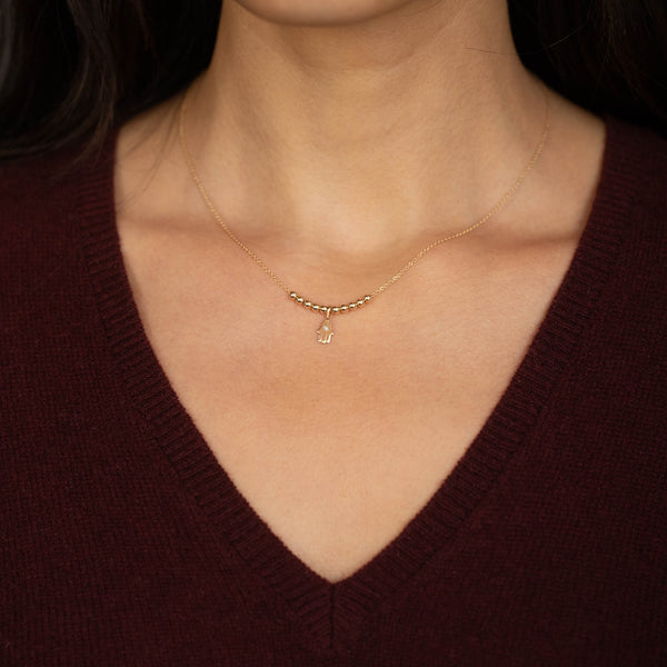 woman in a maroon sweater wearing a Zoë Chicco 14k Gold Bead & Diamond Hamsa Pendant Necklace