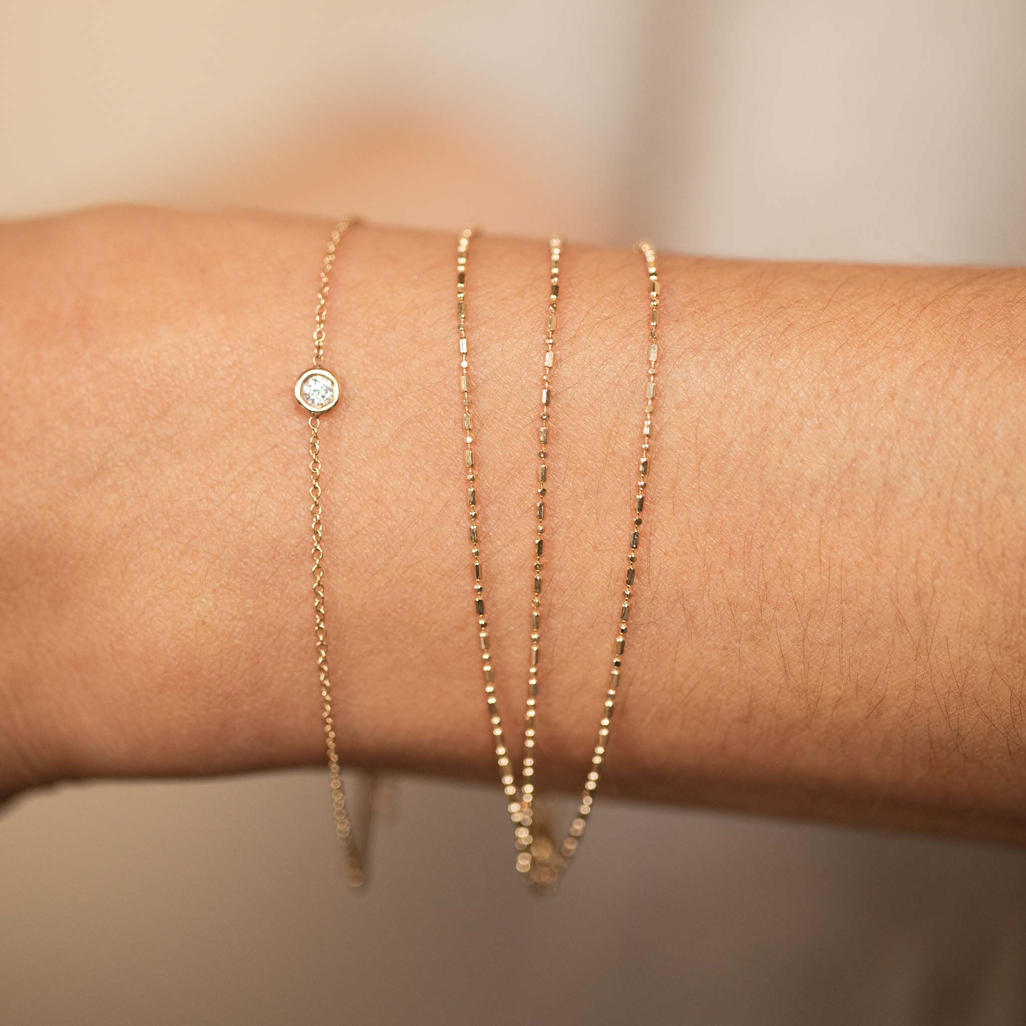 close up of a woman's wrist wearing a Zoë Chicco 14k Gold Triple Strand Tube Bar Chain Bracelet stacked with a Floating Diamond Solitaire Bracelet