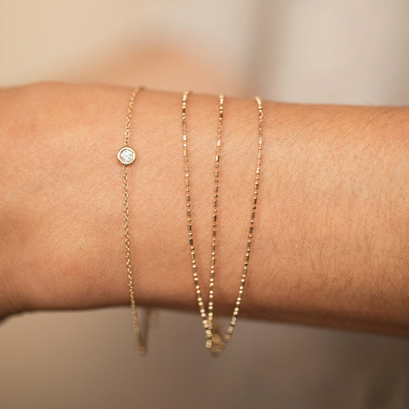 close up of a woman's wrist wearing a Zoë Chicco 14k Gold Triple Strand Tube Bar Chain Bracelet stacked with a Floating Diamond Solitaire Bracelet