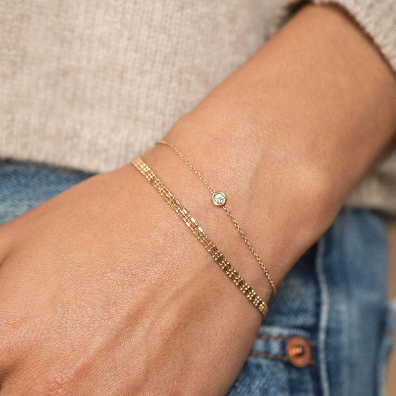 close up of a woman's wrist wearing a Zoë Chicco 14k Gold Triple Strand Tube Bar Chain Bracelet stacked with a Floating Diamond Solitaire Bracelet
