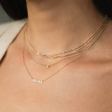 close up of woman's neck wearing a Zoë Chicco 14k Gold Triple Strand Tube Bar & Bead Chain Necklace layered with a Floating Diamond Solitaire Necklace and an Itty Bitty MAMA Necklace