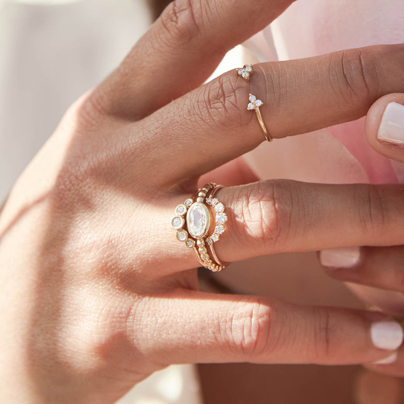 close up of a woman's hand holding a pink flower wearing a Zoë Chicco 14k Gold Graduated Prong Diamond Curved Bar Ring stacked with a one of a kind Oval Rose Cut Diamond Ring and a Graduated Diamond Bezel Ring on her ring finger and a Prong Diamond Trio Open Ring on her middle finger
