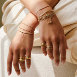 woman sitting down with hands crossed on lap wearing a Zoë Chicco 14k Gold Single Emerald Cut Diamond Cuff Bracelet layered with two other bracelets on one arm
