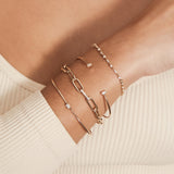 close up of a woman's wrist wearing a Zoë Chicco 14k Gold Baguette Diamond Link Large Paperclip Chain Bracelet layered with three other diamond bracelets