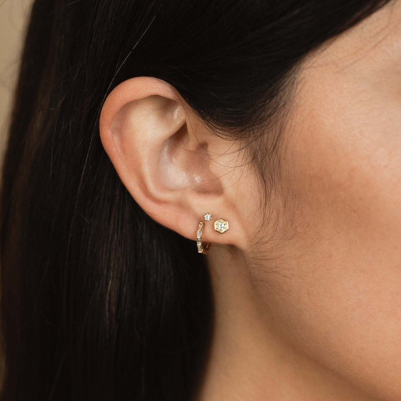 woman's ear wearing a Zoë Chicco 14k Gold Diamond Hexagon Stud Earring layered with a baguette diamond huggie hoop