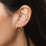 woman's ear wearing a Zoë Chicco 14k Gold Medium Hinge Huggie Hoop with Dangling Diamond Trio layered with a 14k Gold Bamboo Huggie Hoop