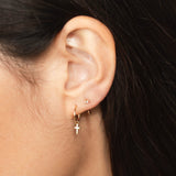 close up of a woman's ear wearing a Zoë Chicco 14k Gold Dangle Itty Bitty Cross Charm Huggie Hoop Earring and a Prong Diamond Reverse Huggie Hoop
