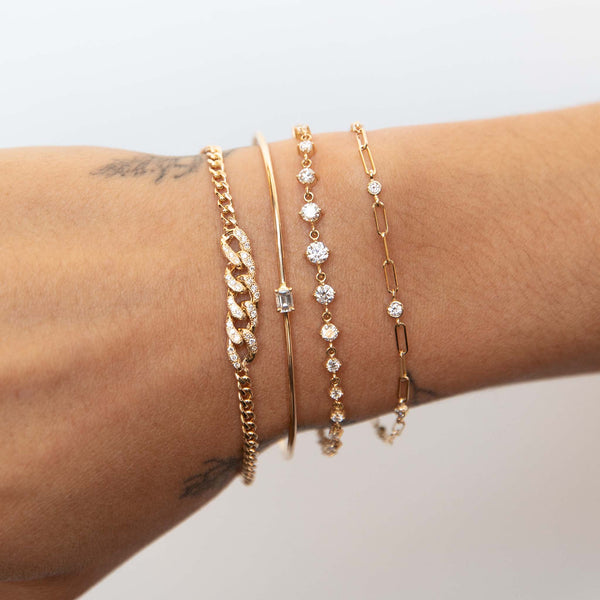 close up of a woman's wrist against a white background wearing a Zoë Chicco 14k Gold Graduated Diamond Bezel Small Paperclip Chain Bracelet layered with three other bracelets