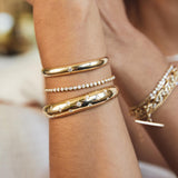 close up of woman's wrist wearing a Zoë Chicco 14k Gold Medium Diamond Bezel Tennis Bracelet stacked with a Star Set Diamond Small Aura Cuff and a Scattered Diamond Medium Aura Cuff Bracelet