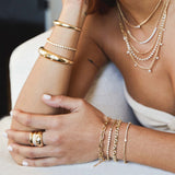 woman resting her arm on the edge of a couch wearing a Zoë Chicco 14k Gold Diamond Tennis Segment Small Curb Chain Bracelet on her wrist layered with three other bracelets