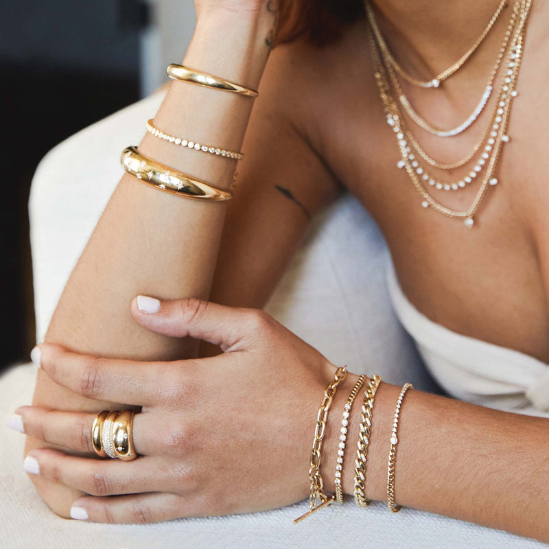 woman resting her arm on the edge of a couch wearing a Zoë Chicco 14k Gold & Alternating Pavé Diamond Medium Curb Chain Bracelet on her wrist