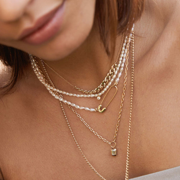 close up of a woman wearing a Zoë Chicco 14k Gold Small Square Oval Link Chain with Emerald Cut Diamond Pendant Necklace layered with two seed pearl necklaces and a curb chain station necklace