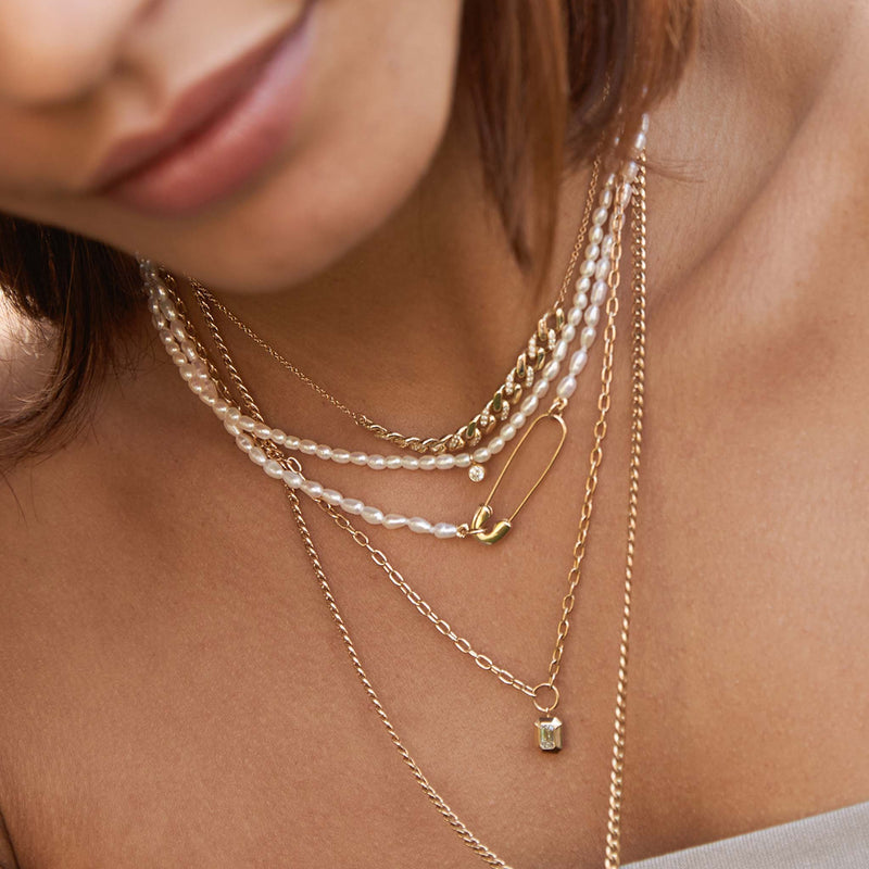 close up of a woman wearing a Zoë Chicco 14k Gold Safety Pin Rice Pearl Necklace layered with multiple other pearl and gold necklaces