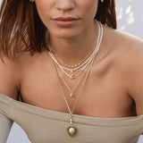 woman in an olive off shoulder top wearing a Zoë Chicco 14k Gold Safety Pin Rice Pearl Necklace layered with multiple other pearl and gold necklaces