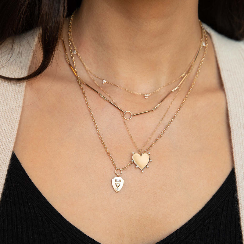 woman wearing a Zoë Chicco 14k Gold 5 Graduated Diamond Trio Station Necklace layered with a 14k 7 Prong Diamond Heart Pendant Necklace and a 14k Mixed Cut Diamond Brushed Gold Shield Pendant Necklace