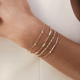 close up of a woman's wrist wearing a Zoë Chicco 14k Gold 3 Diamond Trio Station Bracelet layered with three other diamond bracelets