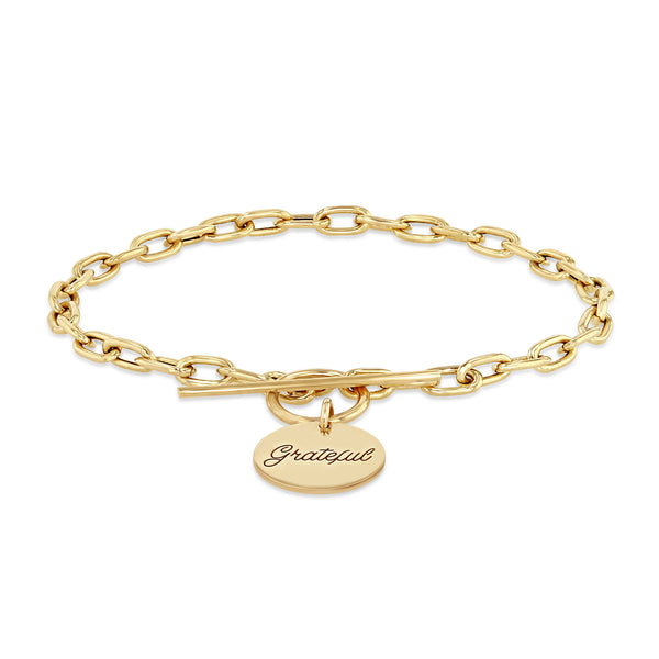 Zoë Chicco 14k Gold Amore Charm Medium Square Oval Link Toggle Bracelet laying down on a white background