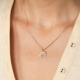 woman in beige knit top wearing a Zoë Chicco 14k Gold Amore Disc Extra Small Curb Chain Necklace engraved with sweet heart