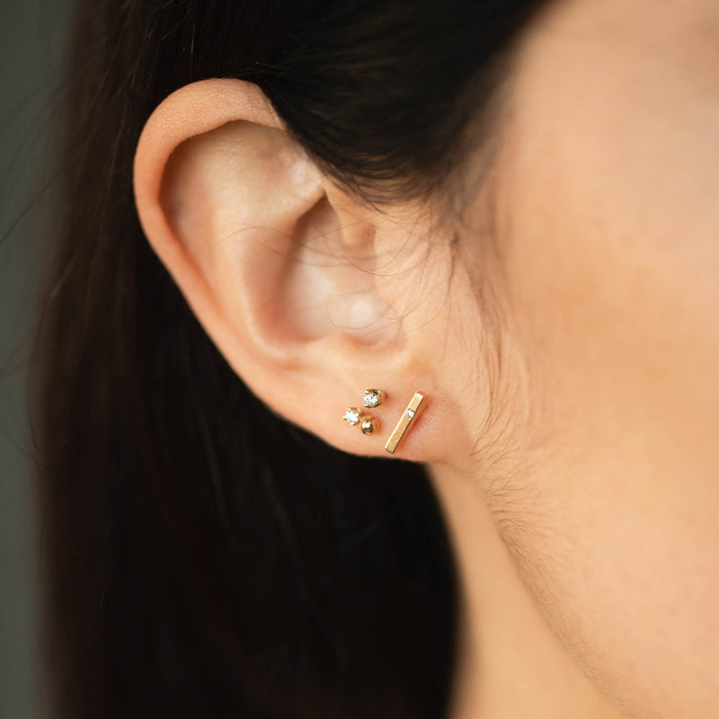 woman's ear wearing a Zoe Chicco 14k Gold Single Diamond Thin Bar Stud Earring layered with a Gold Bead & Diamond Stud