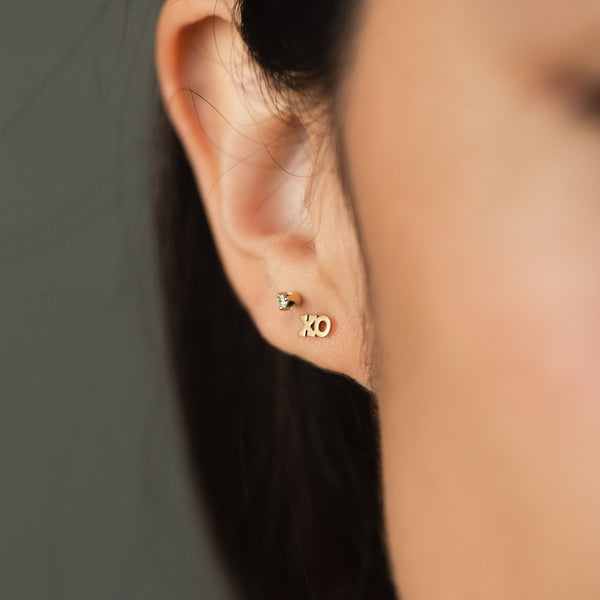 close up of woman's ear wearing a Zoë Chicco 14k Gold Itty Bitty XO Letter Stud Earring 
