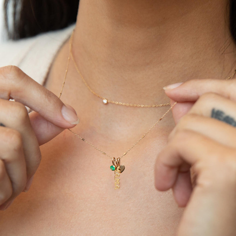 woman holding up a Zoë Chicco 14k Gold MAMA Charm Necklace with Heart & Personalized Emerald Birthstone