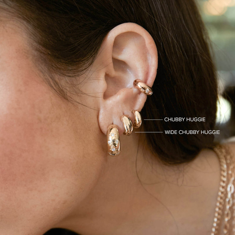 close up of woman's ear wearing Zoë Chicco 14k Gold Chubby Huggie Hoop Earrings and 14k Gold Wide Chubby Huggie Hoop Earrings